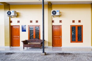 A building with two wooden doors, a bench, and two air conditioning units mounted on the wall. - SPOT ON 2790 Bintang Selatan Syariah (Colomadu)