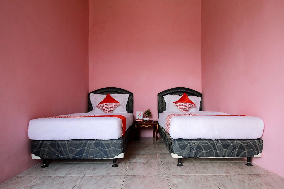 A room with two beds, each with a patterned bedspread and red pillows, against a pink wall.