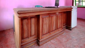 A wooden desk with a computer and a refrigerator in a room with pink walls and tiled floor. - OYO 2838 Hotel Ayu (Bengkulu)