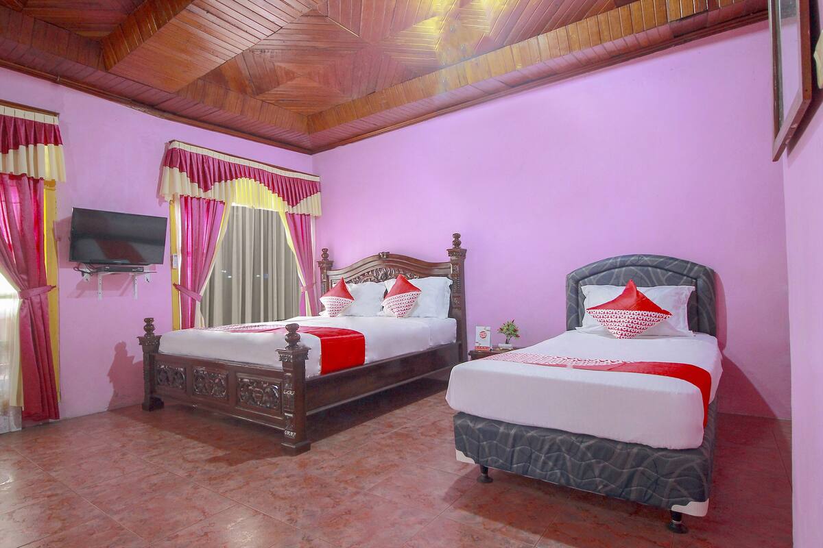 A room with two beds, a TV mounted on the wall, and a wooden ceiling.