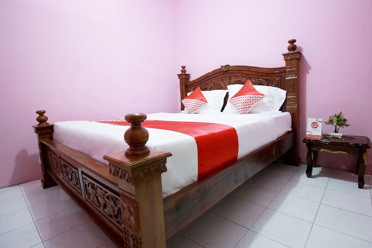 A bed with a wooden headboard, white bedding, and red accents.