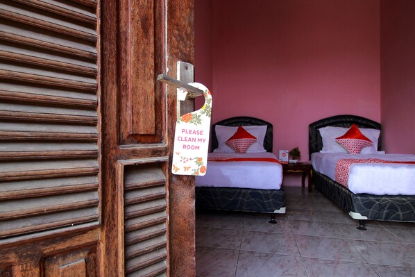A hotel room with two beds, a wooden door, and a sign requesting guests to clean their room.