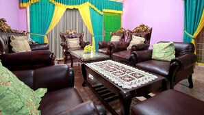 A room with dark brown leather sofas and armchairs, a glass coffee table with a lace table runner, and a green door with yellow curtains. - OYO 2838 Hotel Ayu (Bengkulu)