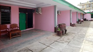 A building with pink walls, green doors, and a covered outdoor area with wooden chairs and planters. - OYO 2838 Hotel Ayu (Bengkulu)