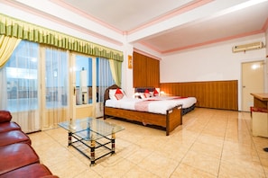 A hotel room with a bed, a glass table, a red leather couch, and a view of the city through large windows. - OYO 2855 Sartika Hotel Pati (Pati)