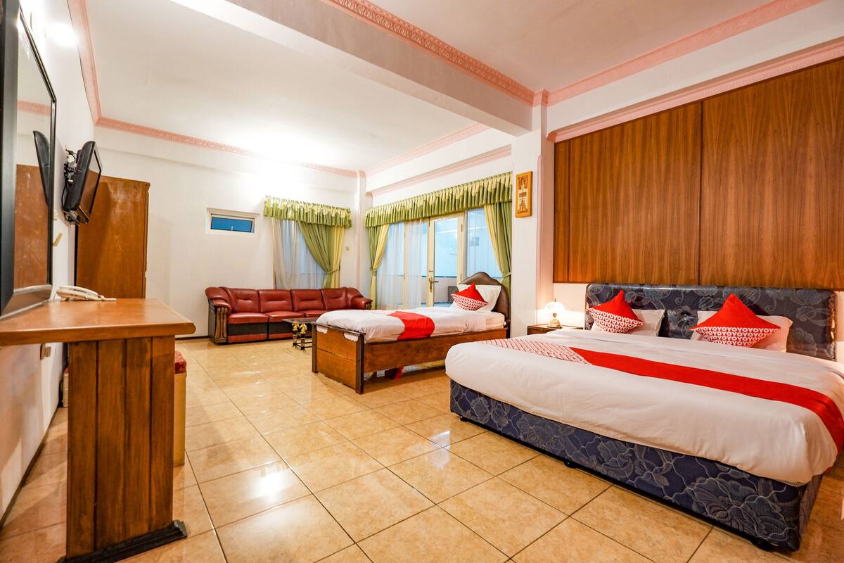 A hotel room with a large bed, a smaller bed, a desk, a red sofa, and a wooden wardrobe.