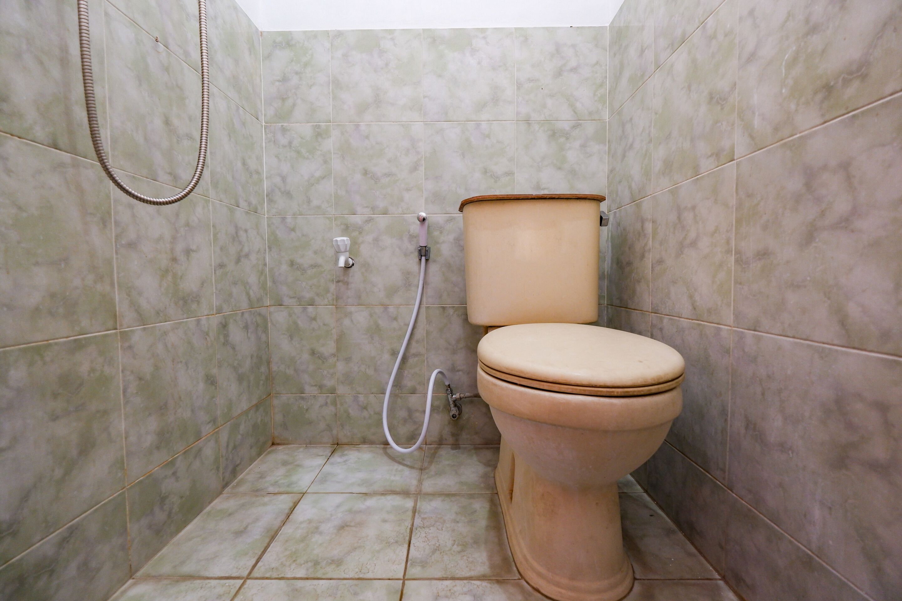 A small bathroom with a toilet, a shower hose, and a toilet paper holder.