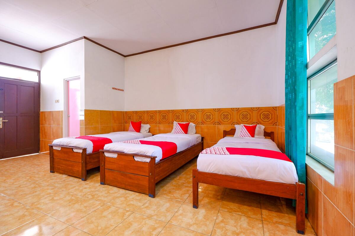A hotel room with three wooden beds, each with white bedding and red accents.