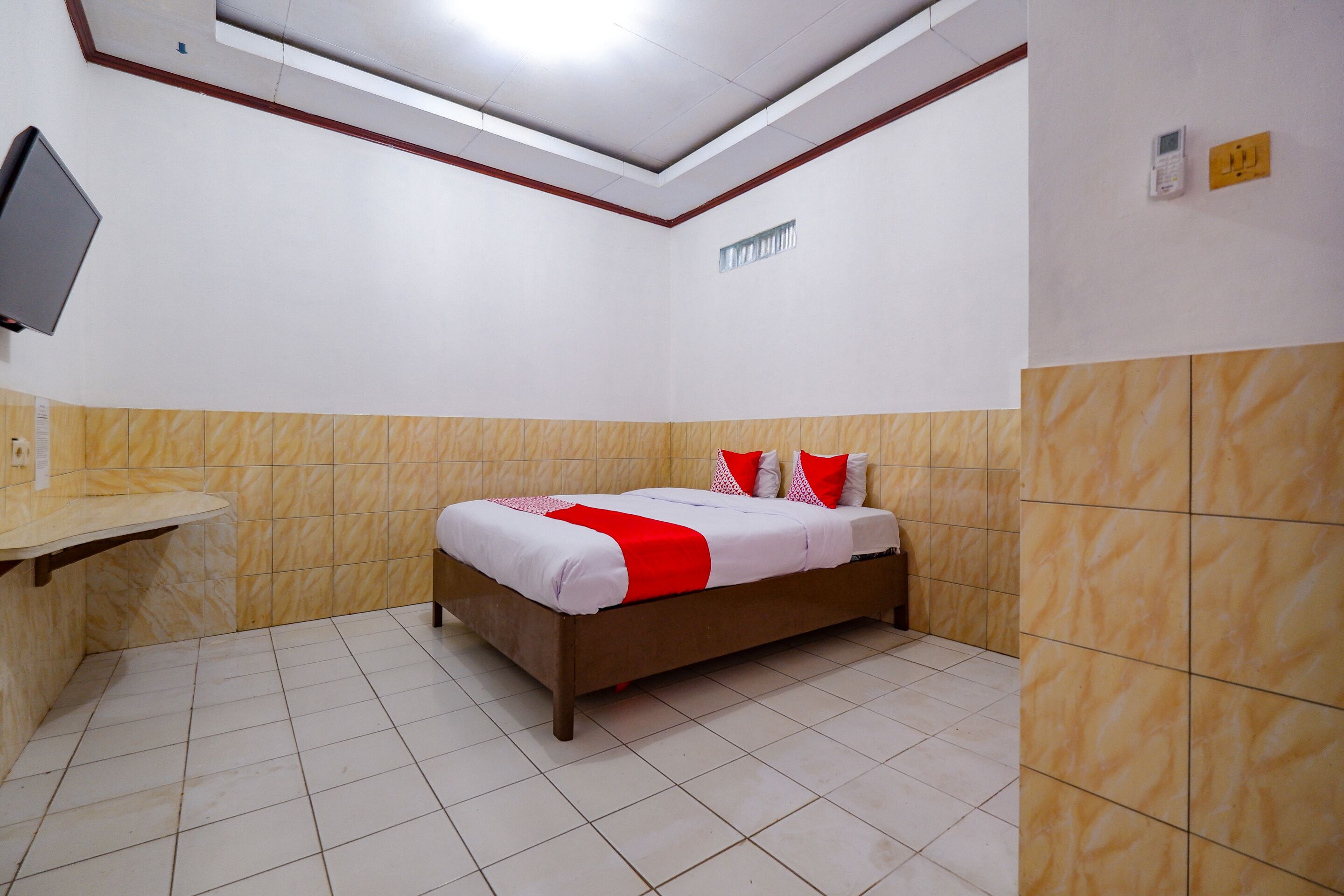A hotel room with a bed, a TV mounted on the wall, and a small window.