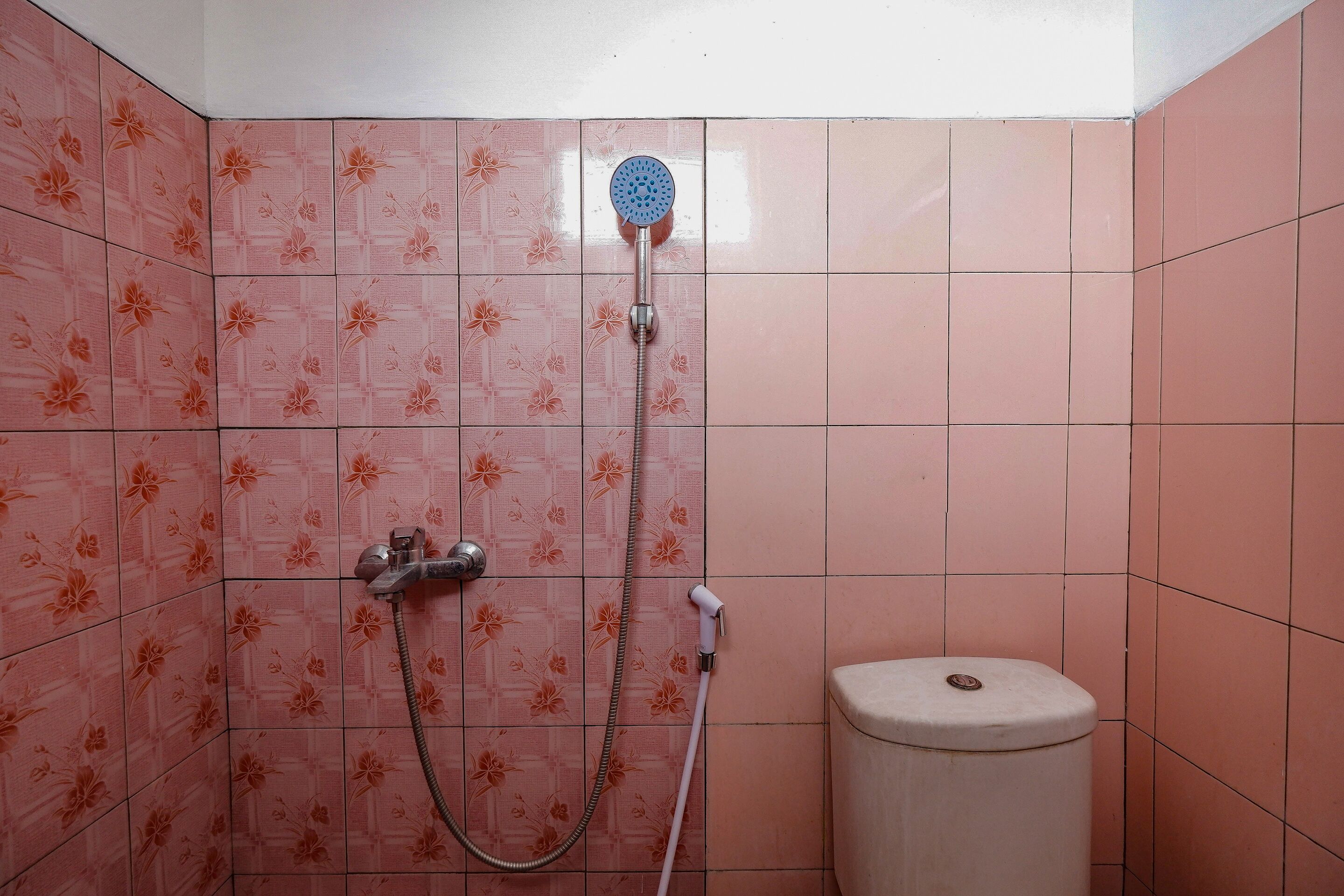 Um banheiro com azulejos florais cor-de-rosa, um chuveiro, um chuveirinho e um vaso sanitário.