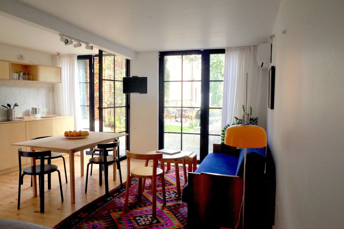 A modern kitchen with a dining area, large windows, and a TV.