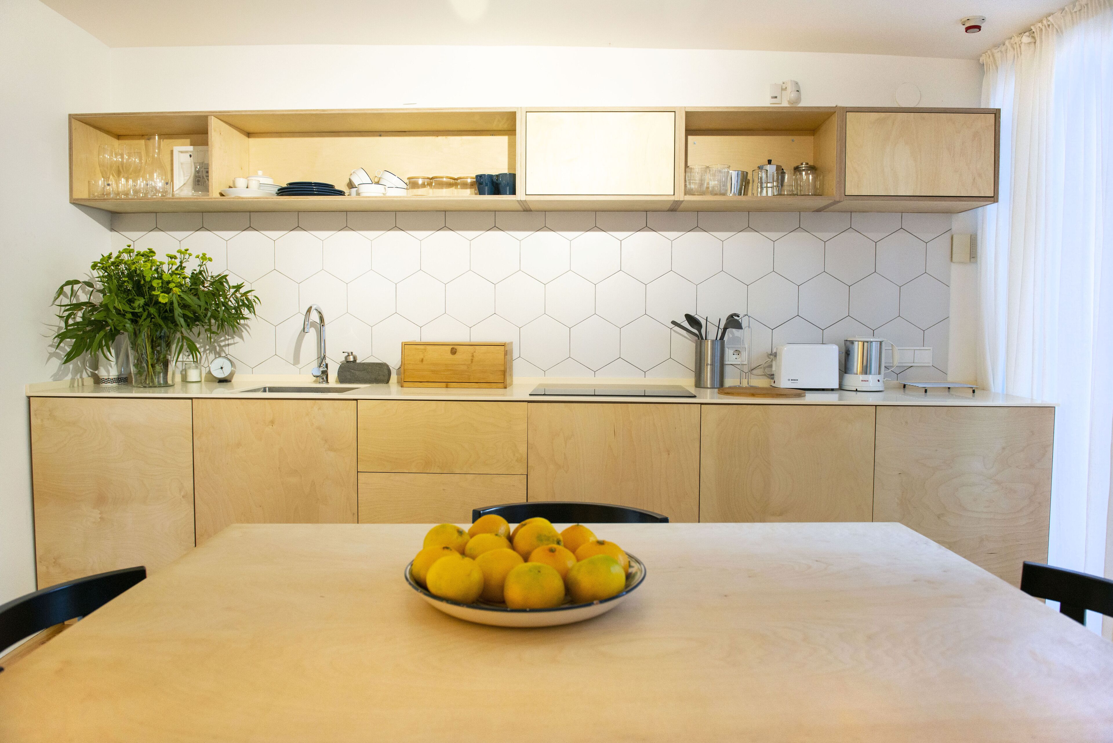 Una cocina moderna con armarios de madera, un respaldas de azulejos hexagonales y una mesa de comedor con un tazón de fruta.