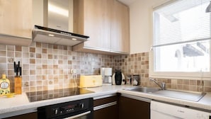 A modern kitchen with a dishwasher, oven, and a window with blinds. - Vacation home Hélios by Interhome (Port Camargue)