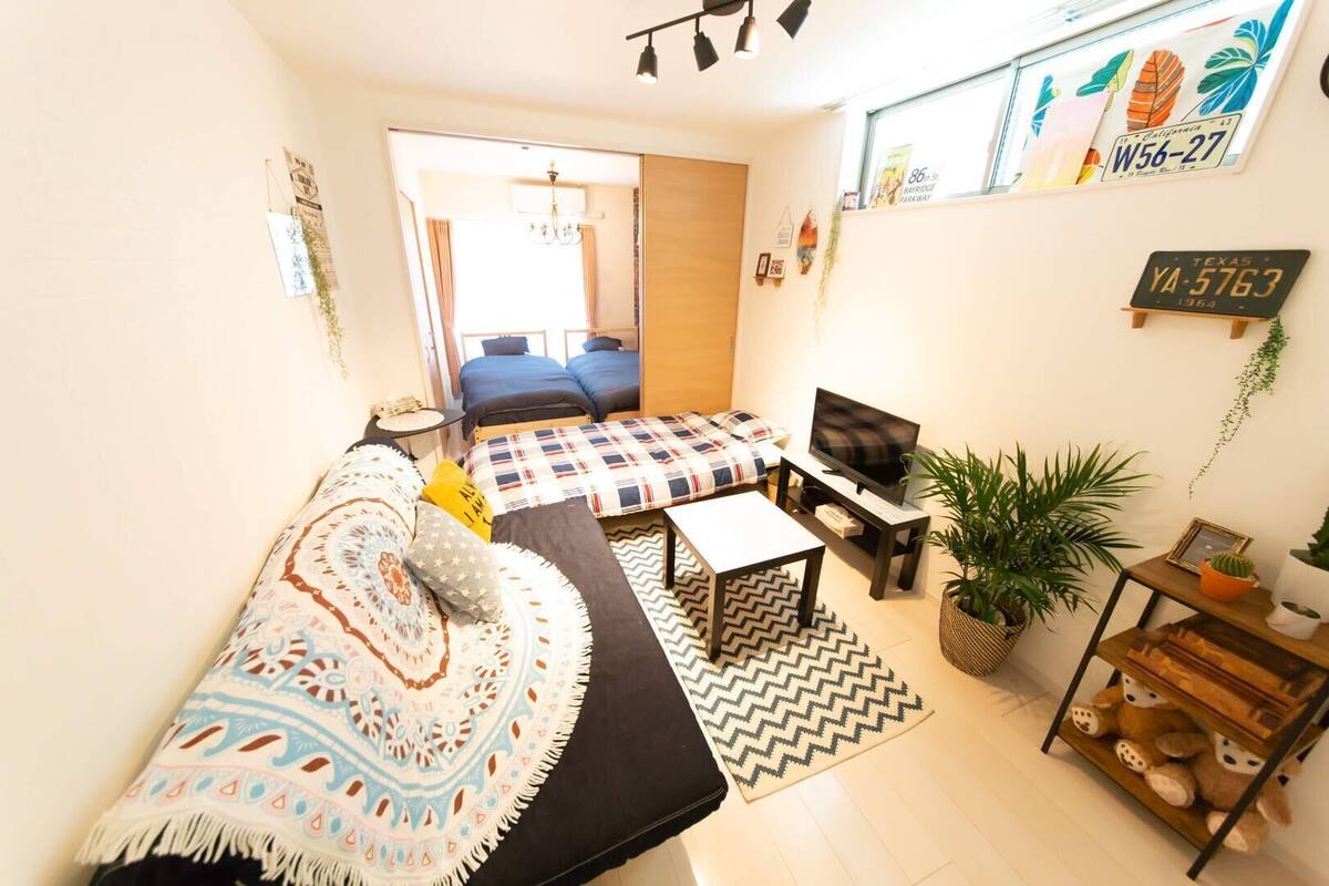 A cozy room with a sofa, a bed, a TV, and a small table. There are plants and a sign on the wall.