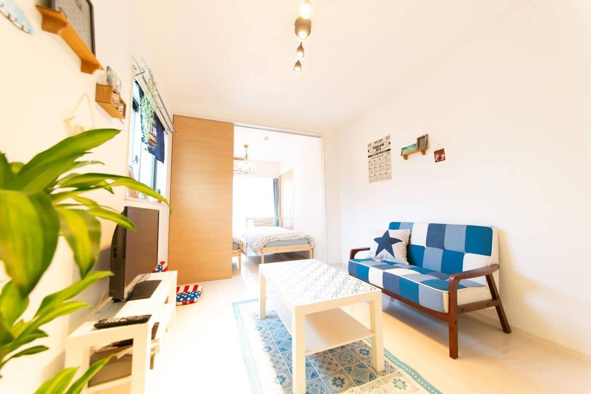 A compact living space with a sofa, a small table, a TV, and a bed in the background.