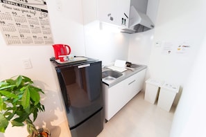 Una cocina compacta con un refrigerador negro, un lavamanos y una estufa. Hay un calendario en la pared y una planta en la esquina.