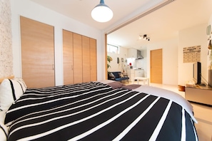 Un dormitorio con una cama grande, un armario de madera, un escritorio pequeño y una kitchenette al fondo.