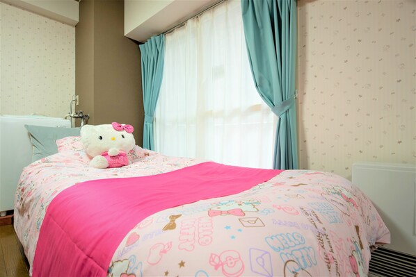 A bedroom with a bed, a Hello Kitty plush toy, a pink bedspread, and a window with curtains.