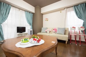A modern living room with a wooden dining table, a sofa with Hello Kitty decorations, and a TV on a stand.
