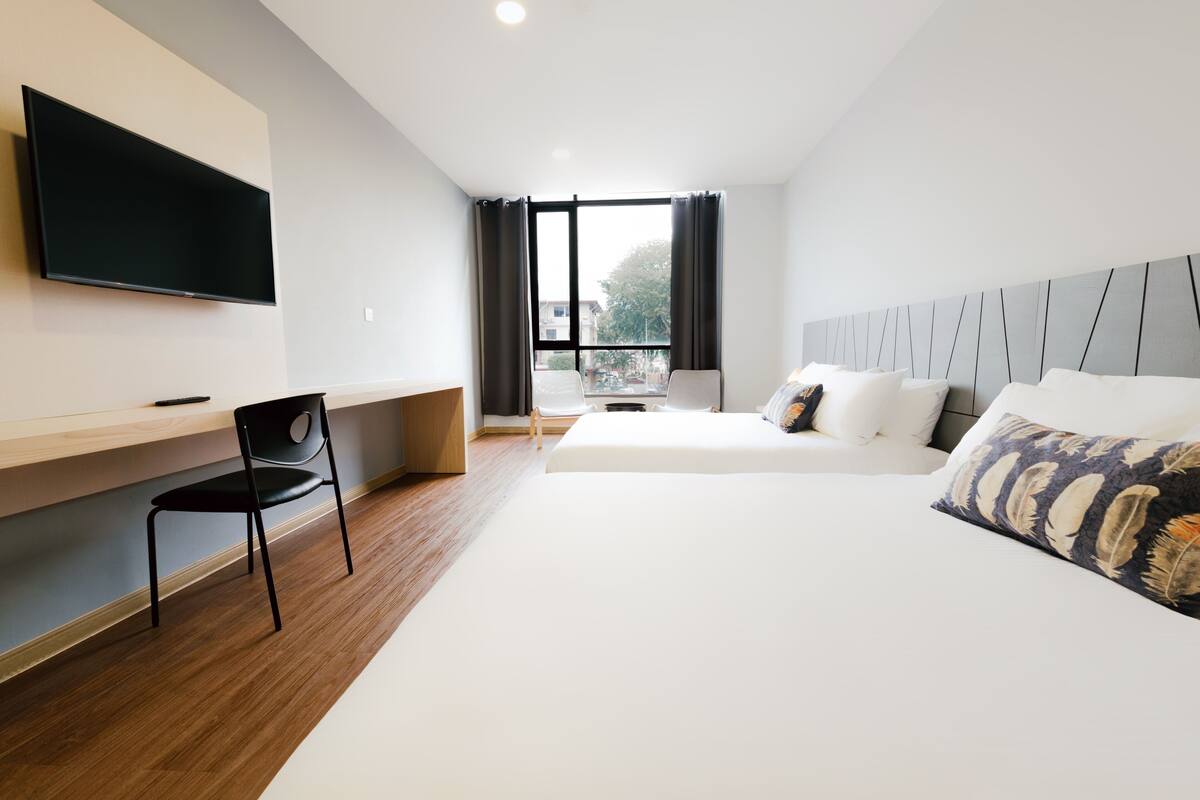 Ein modernes Hotelzimmer mit einem großen Bett, einem Schreibtisch, einem Sessel, einem Flachbildfernseher und einem Fenster mit Vorhängen.