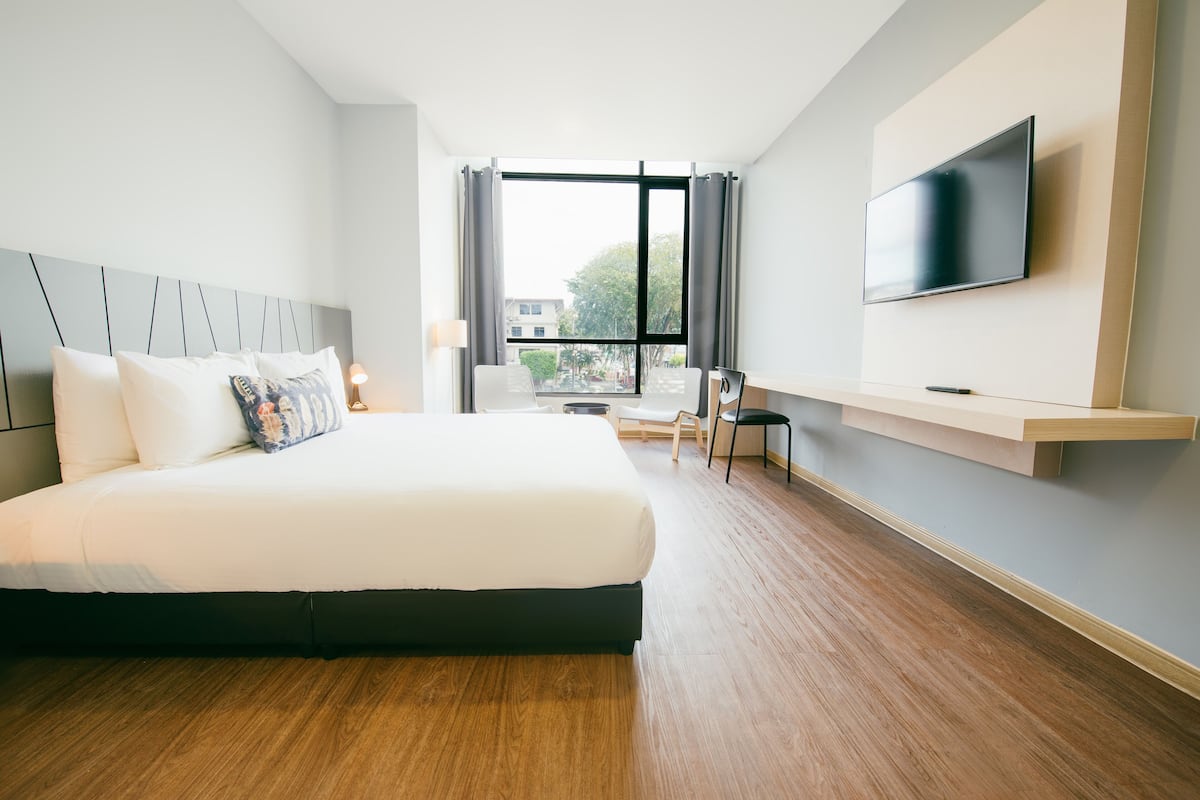 Ein modernes Hotelzimmer mit einem großen Bett, einem an der Wand befestigten Fernseher und Blick ins Freie durch ein großes Fenster.