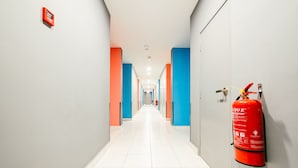 A hallway with alternating blue and orange walls, white tiled floors, and a red fire extinguisher mounted on the wall. - Signature by The Concept (Langkawi)