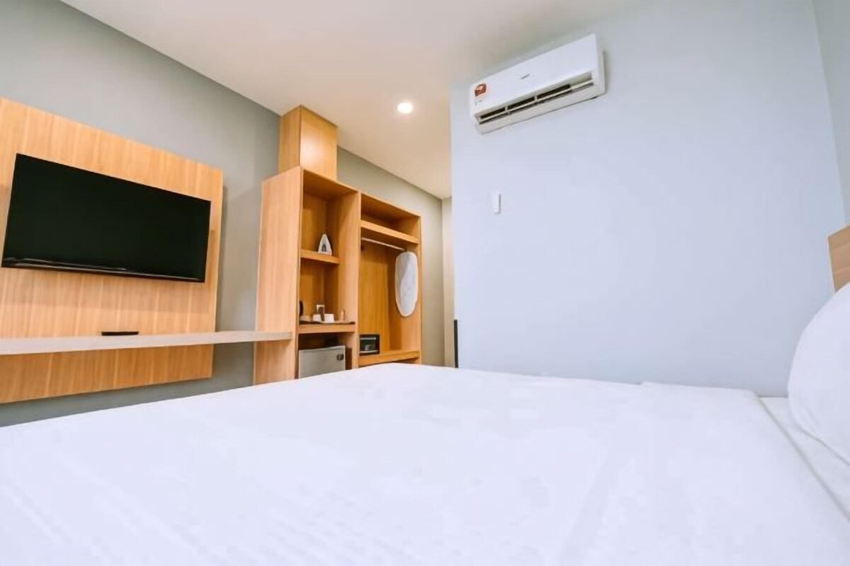 A hotel room with a bed, a TV mounted on the wall, a built-in shelf unit, and an air conditioning unit.