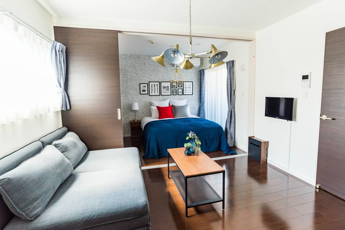A modern hotel room with a sofa, a bed with a blue bedspread, a wooden table, and a ceiling fan.