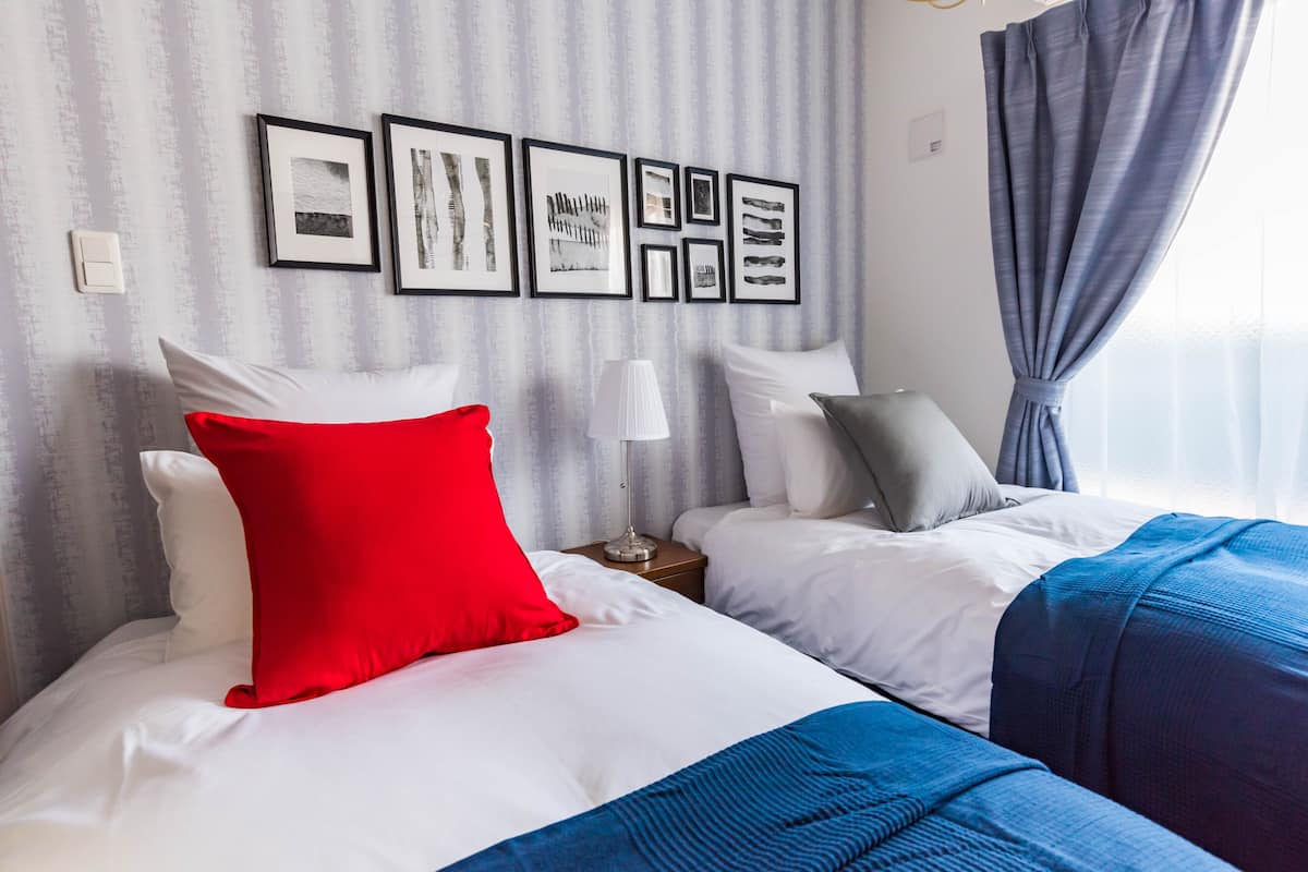 A hotel room with two beds, a red pillow, a lamp, and framed pictures on the wall.