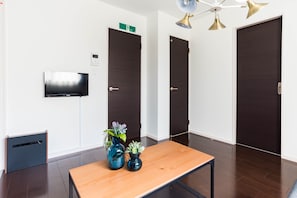A hotel room with a wooden table, two dark doors, a TV mounted on the wall, and a small plant on the table.