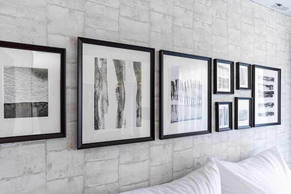 A wall with framed artwork and a white bed with white bedding.