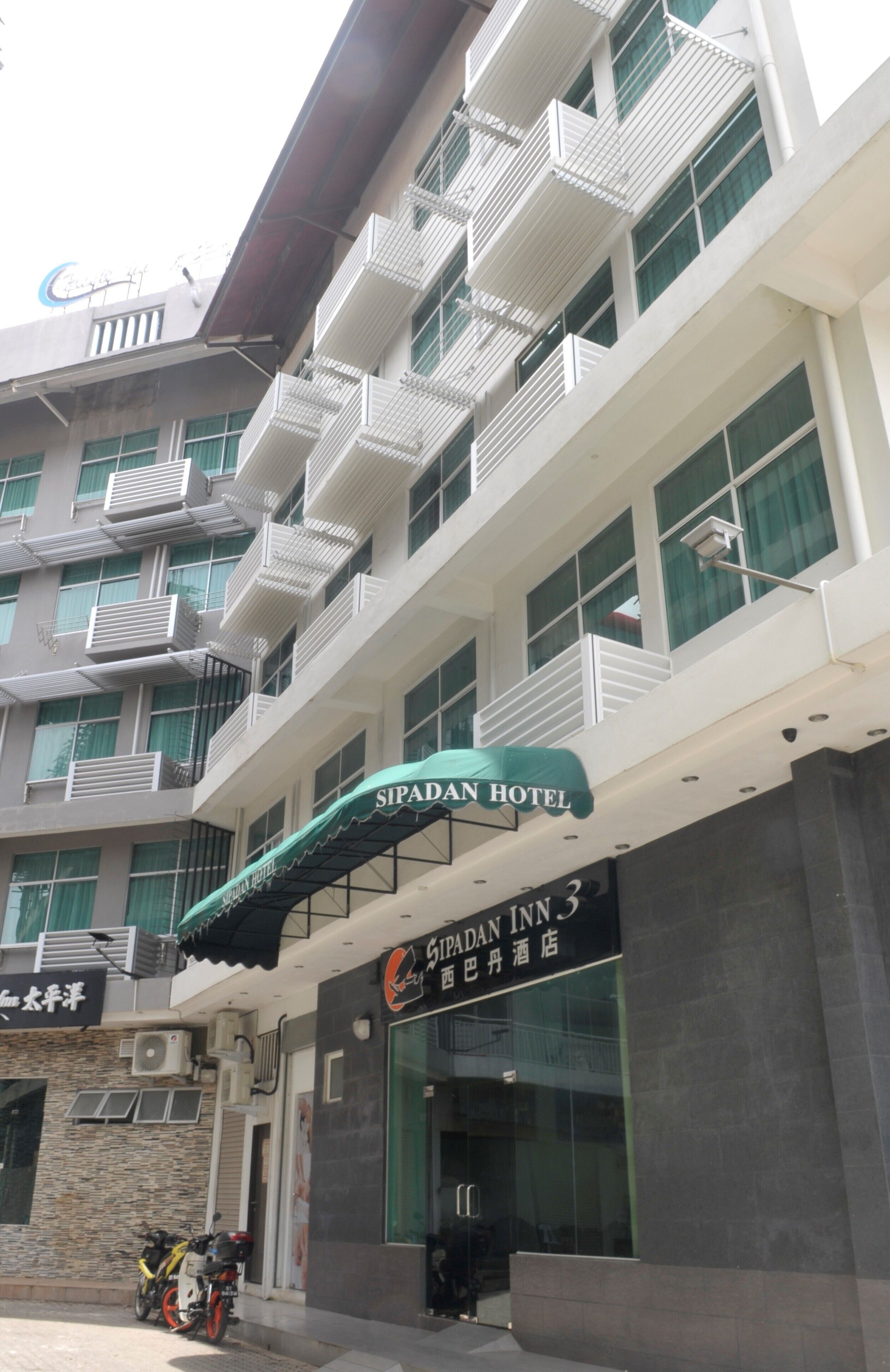 A multi-story building with balconies, a sign for 'Sipadan Hotel', and a 'Gipadan Inn 3' sign.
