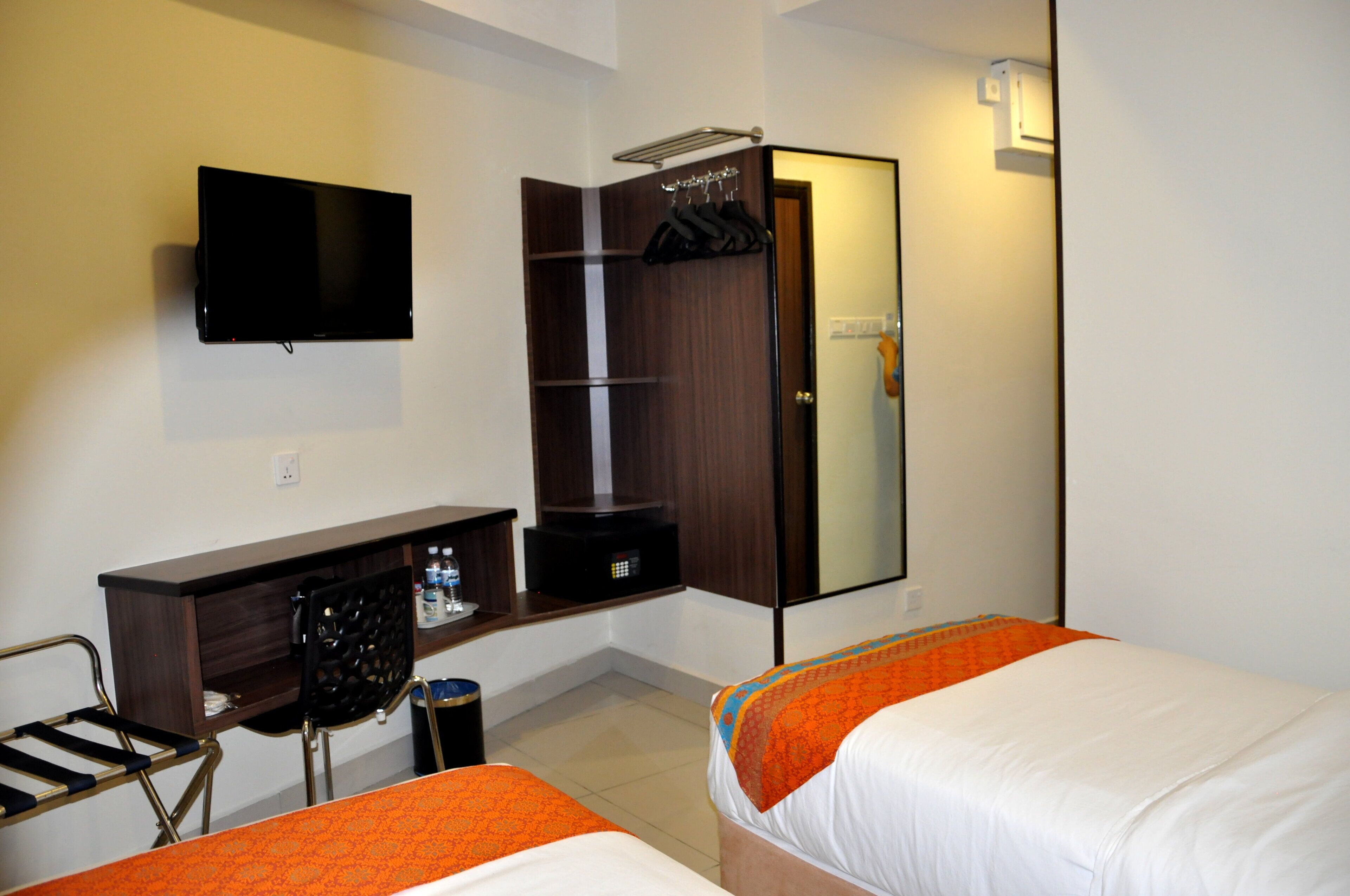 A hotel room with a bed, a desk with a chair, a TV mounted on the wall, and a wardrobe.