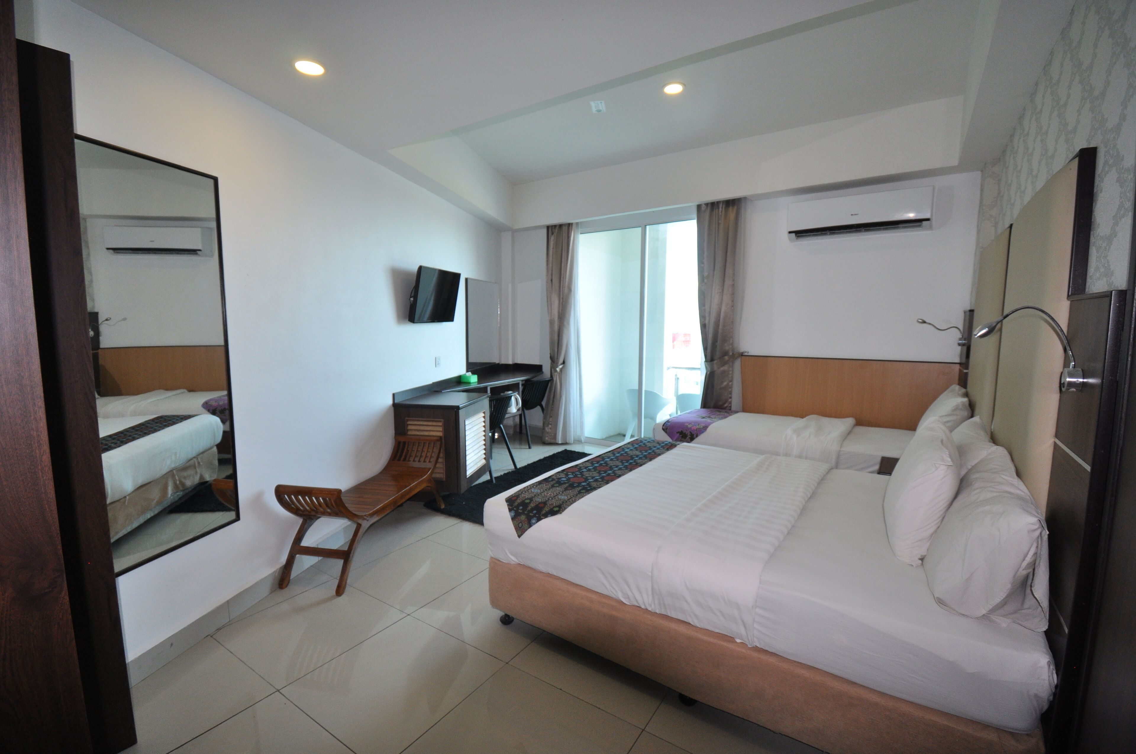 A hotel room with a large bed, a desk with a chair, a television, and an air conditioning unit.