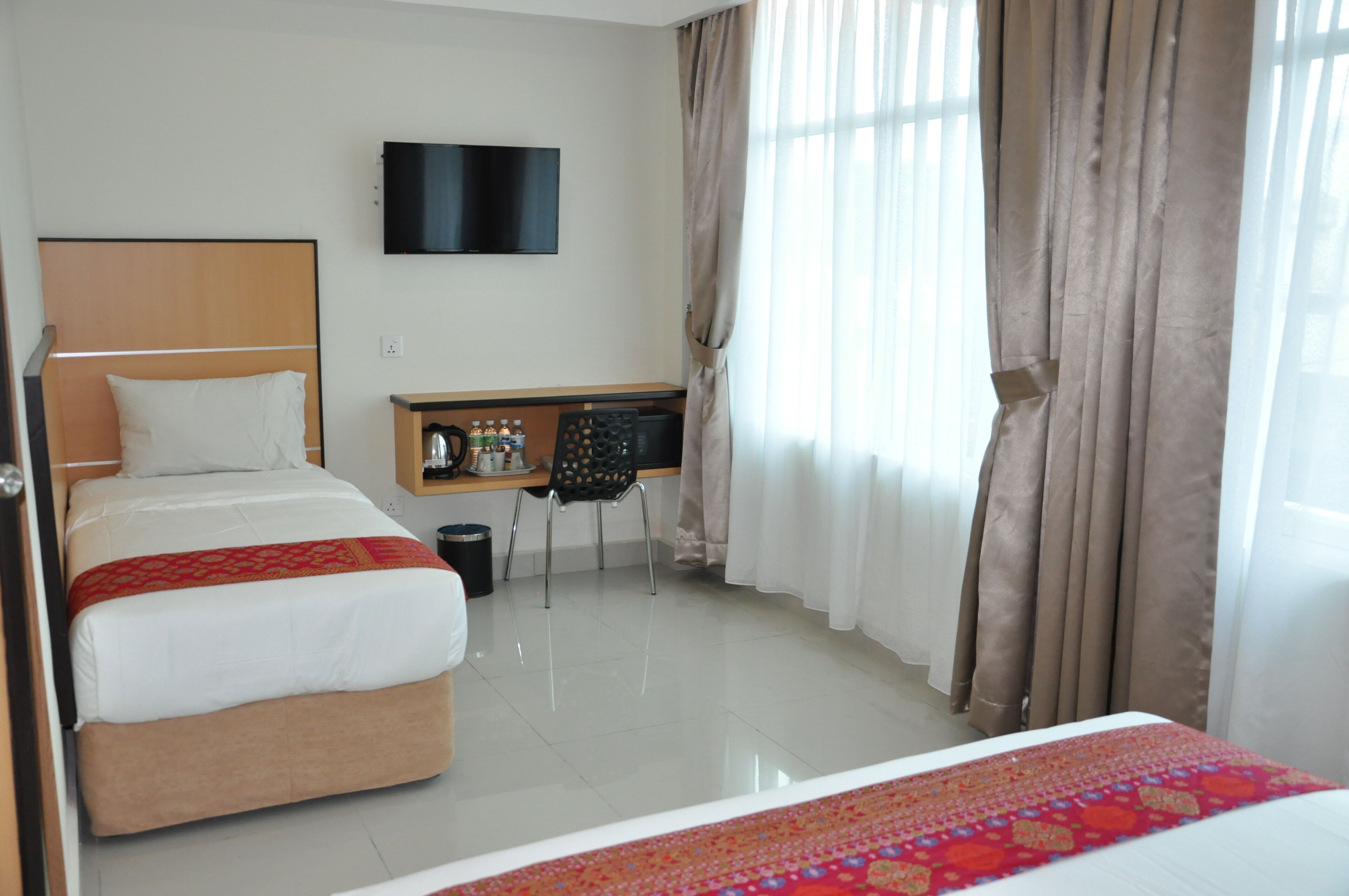 A hotel room with two beds, a desk with a chair, a television, and a window with curtains.