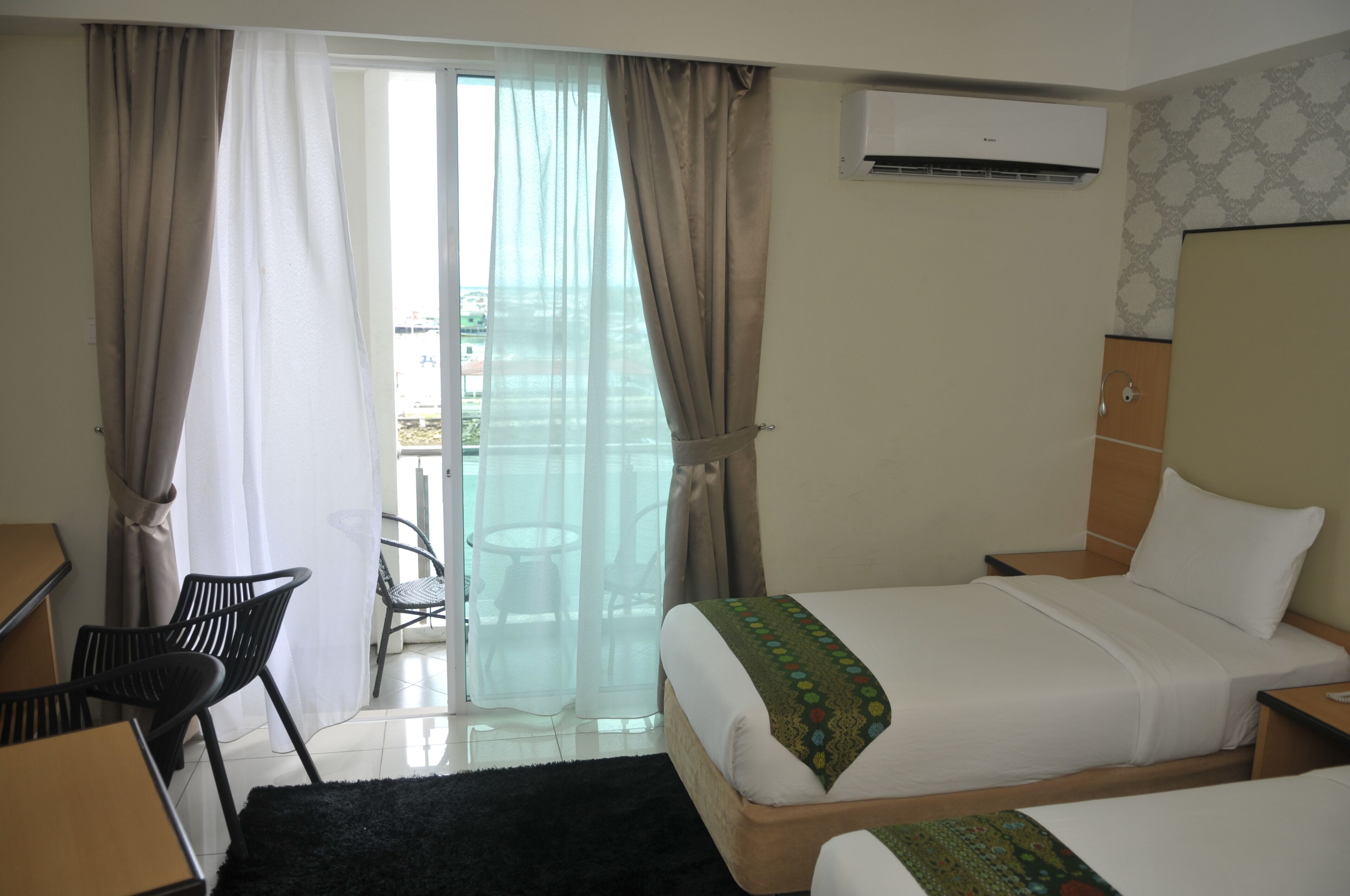A hotel room with a bed, a desk, a chair, and a balcony with curtains.