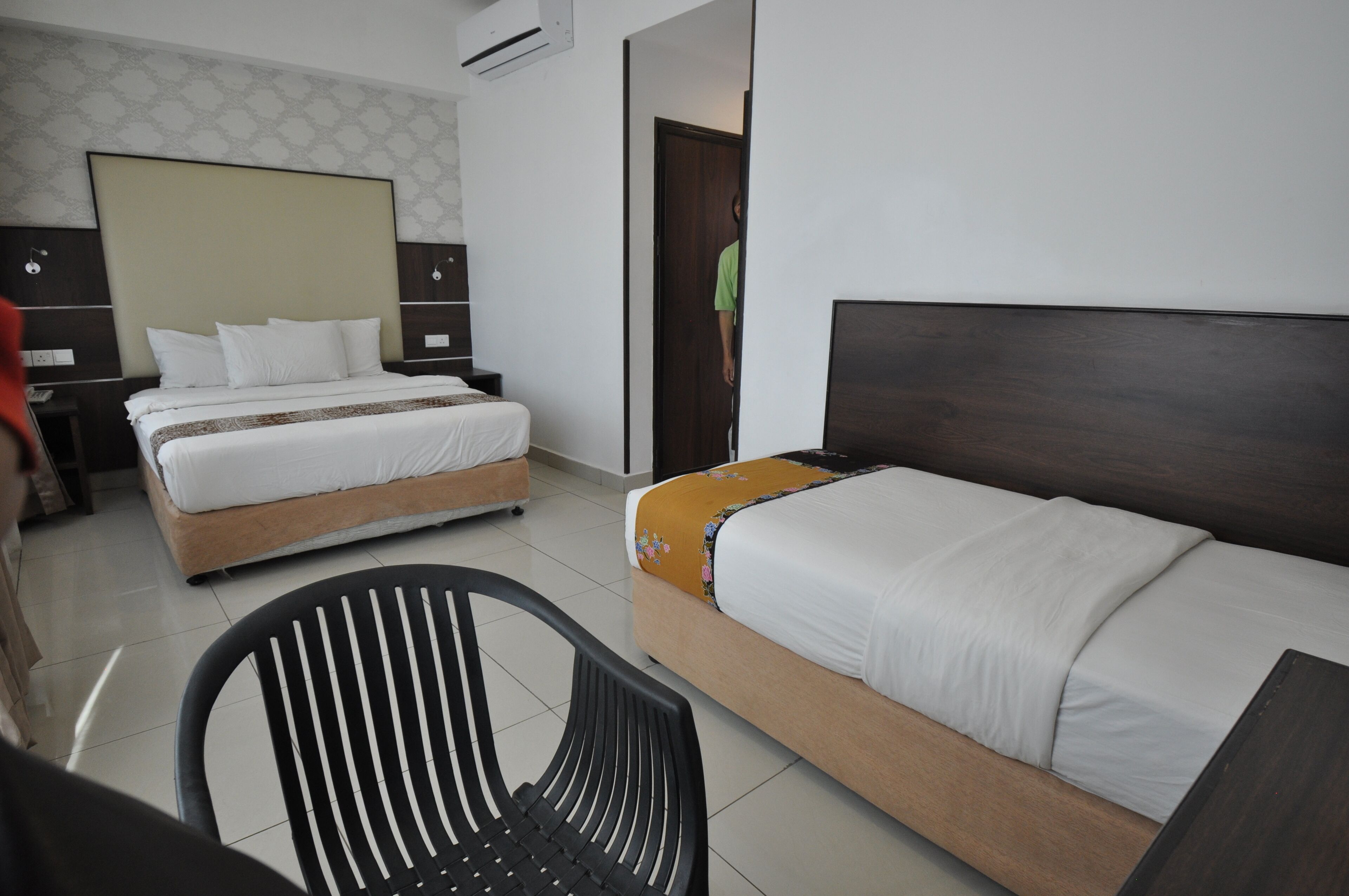 A hotel room with two beds, a wooden headboard, a black chair, and a patterned wall.