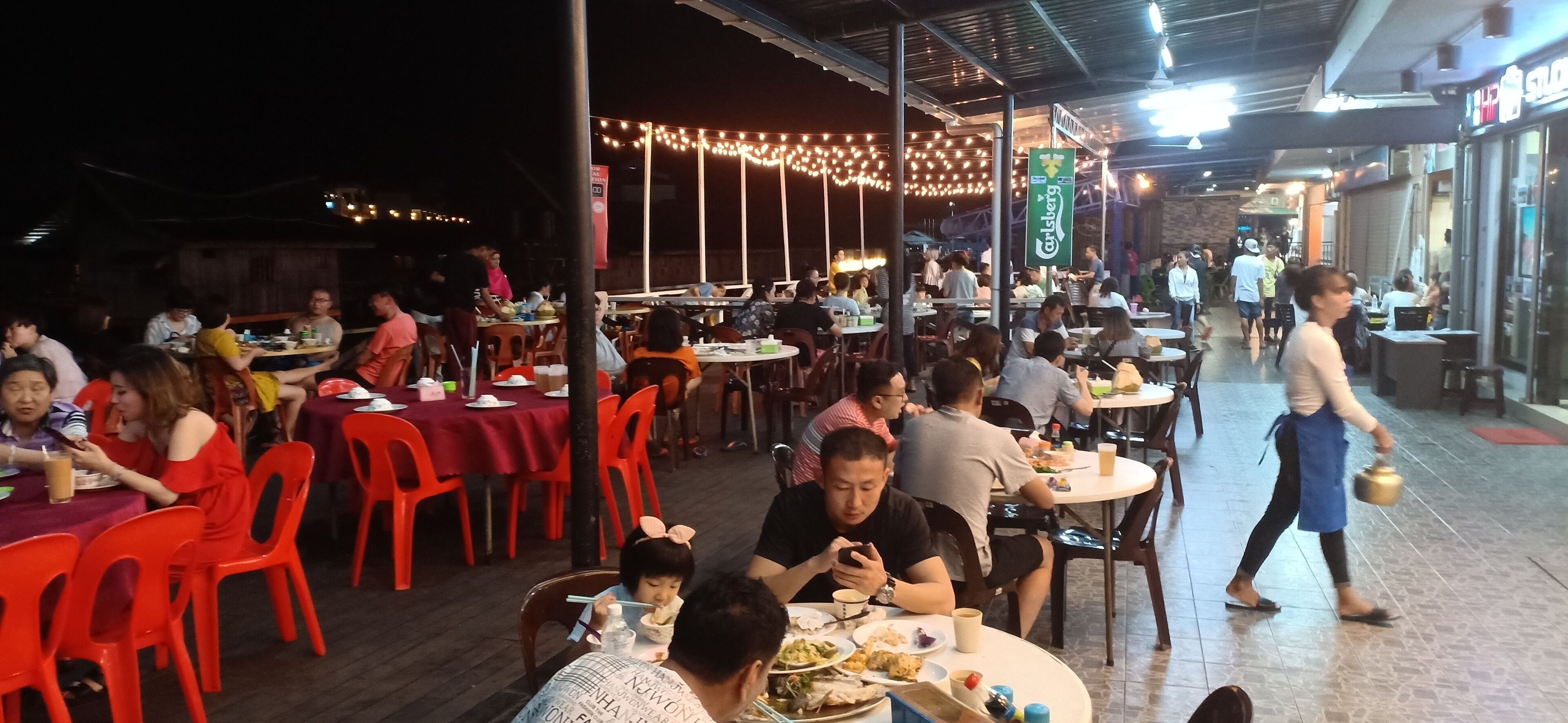 An outdoor dining area with tables and chairs, string lights, and people dining.