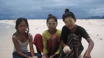 Three individuals sitting on a sandy beach with a cloudy sky in the background.