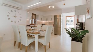 A modern kitchen with white cabinetry, a stainless steel refrigerator, and a dining area with a white table and chairs. - Villa Oriens in Gennadi (Rhodes)