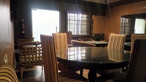 Un coin repas avec une table ronde entourée de chaises à rayures, d’un fauteuil en osier et d’un canapé rembourré.