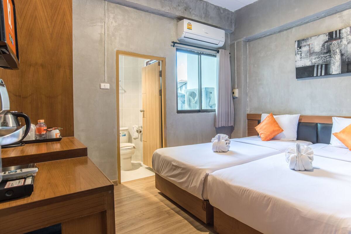 Ein Hotelzimmer mit zwei Betten, einem Holztisch, einem Wasserkocher, einer Flasche und einem Bild an der Wand.