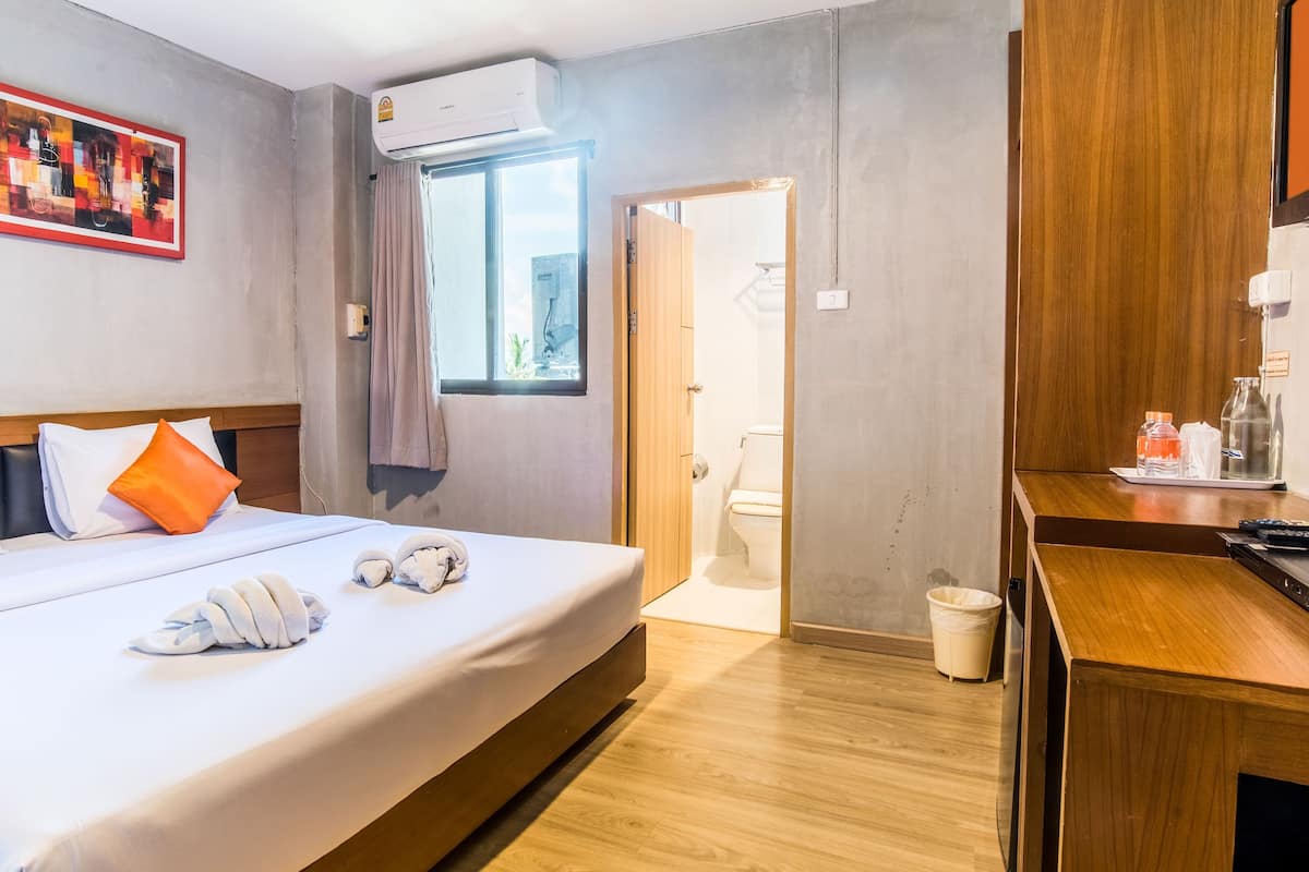 Ein Hotelzimmer mit Bett, Gemälde, Klimaanlage, Schreibtisch aus Holz und einer Badezimmertür.