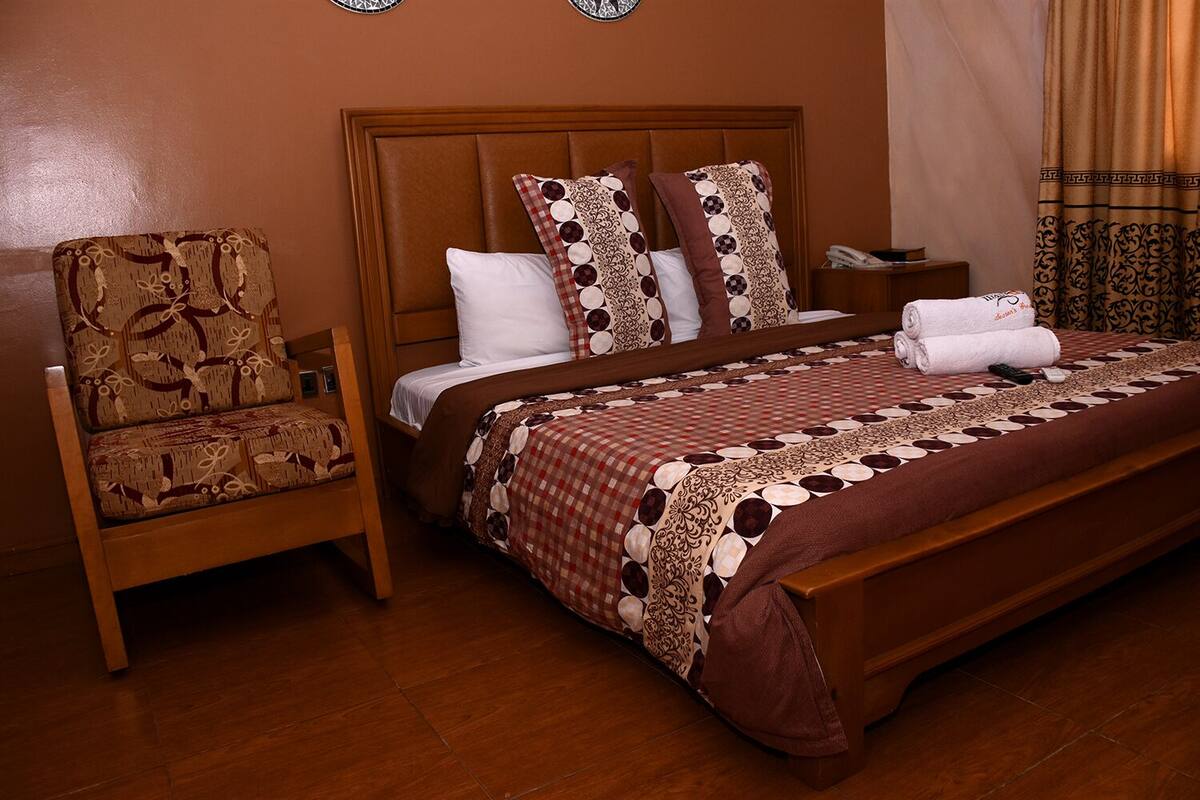 A hotel room with a large bed, a wooden chair, a nightstand, and a wall clock.