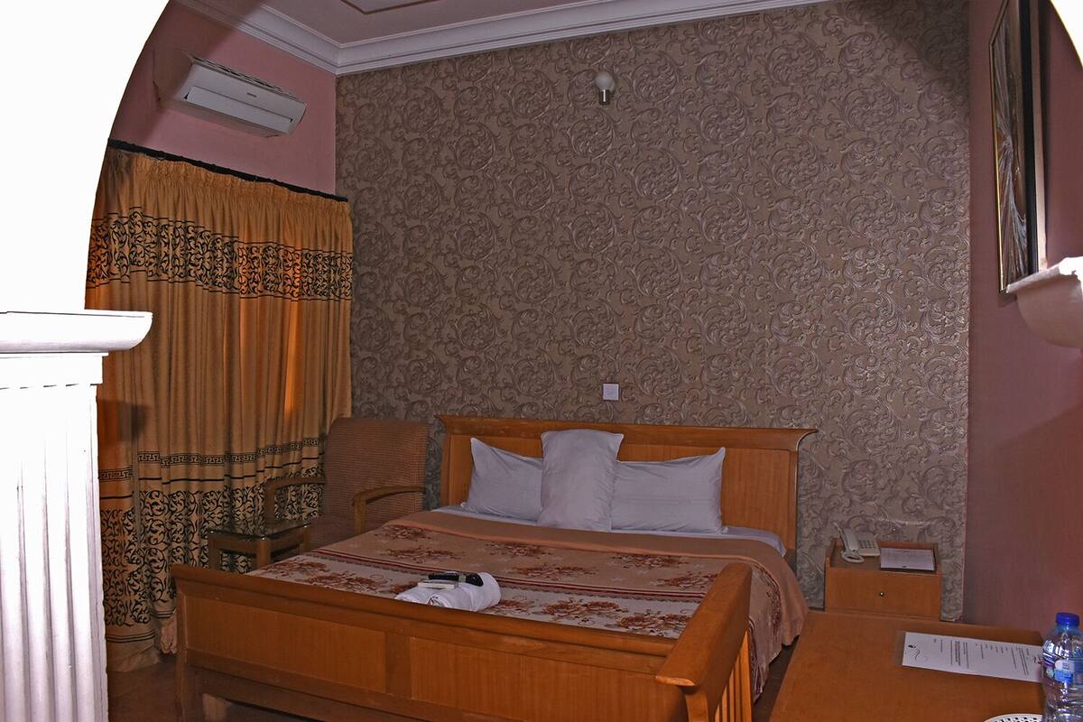 A hotel room with a wooden bed, a nightstand, a telephone, and a water bottle on the nightstand.
