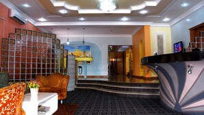 A hotel lobby with a reception desk, a sofa, a coffee table, and a staircase leading to other areas. - LaMaison Hotel (Ibadan)