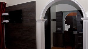 A hotel room with a dark wood panel wall, a white arched doorway leading to a bathroom, and a bed with a dark headboard. - LaMaison Hotel (Ibadan)
