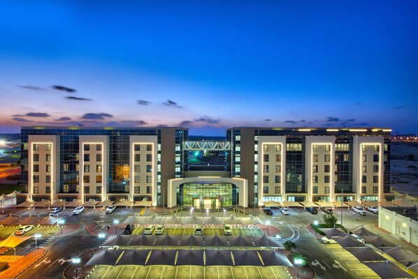Un hotel moderno con fachada de vidrio central, varios niveles de estacionamiento y una entrada bien iluminada.