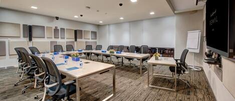 A conference room with multiple tables and chairs, a whiteboard, and a projection screen.