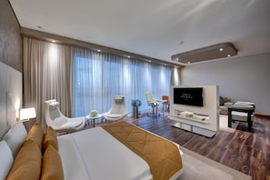 Una habitación de hotel moderna con una cama grande, dos sillones blancos, un televisor y un comedor.